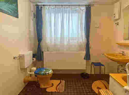 Badezimmer mit orangener Garnitur mit Toilette, Waschbecken, Badewanne und Fenster mit blauen Vorhängen Badezimmer mit orangener Garnitur mit Toilette, Waschbecken, Badewanne und Fenster mit blauen Vorhängen
