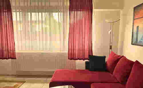 rotes Sofa Weitsicht mit hellem Fenster und roten Gardinen und einer Stehlampe