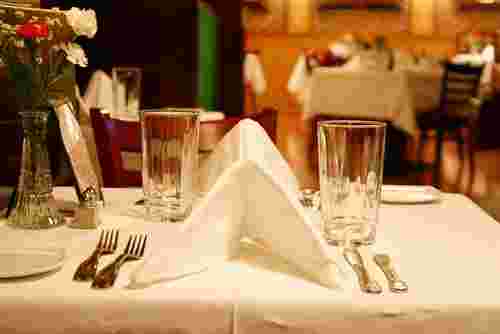 Das Bild zeigt einen festlich gedeckten Tisch in einem Restaurant mit Gläsern, Besteck und einer gefalteten Stoffserviette. Das Bild zeigt einen festlich gedeckten Tisch in einem Restaurant mit Gläsern, Besteck und einer gefalteten Stoffserviette.