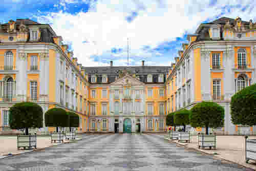 Das Bild zeigt das prachtvolle Schloss Augustusburg in Brühl mit gepflegtem Vorplatz und symmetrischen Bäumen.