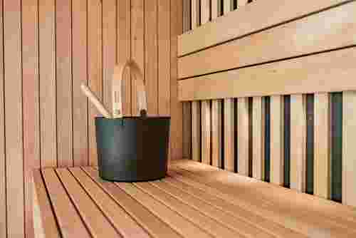 Das Bild zeigt den Innenraum einer modernen Sauna mit Holzverkleidung und einem schwarzen Saunaeimer auf der Bank.
